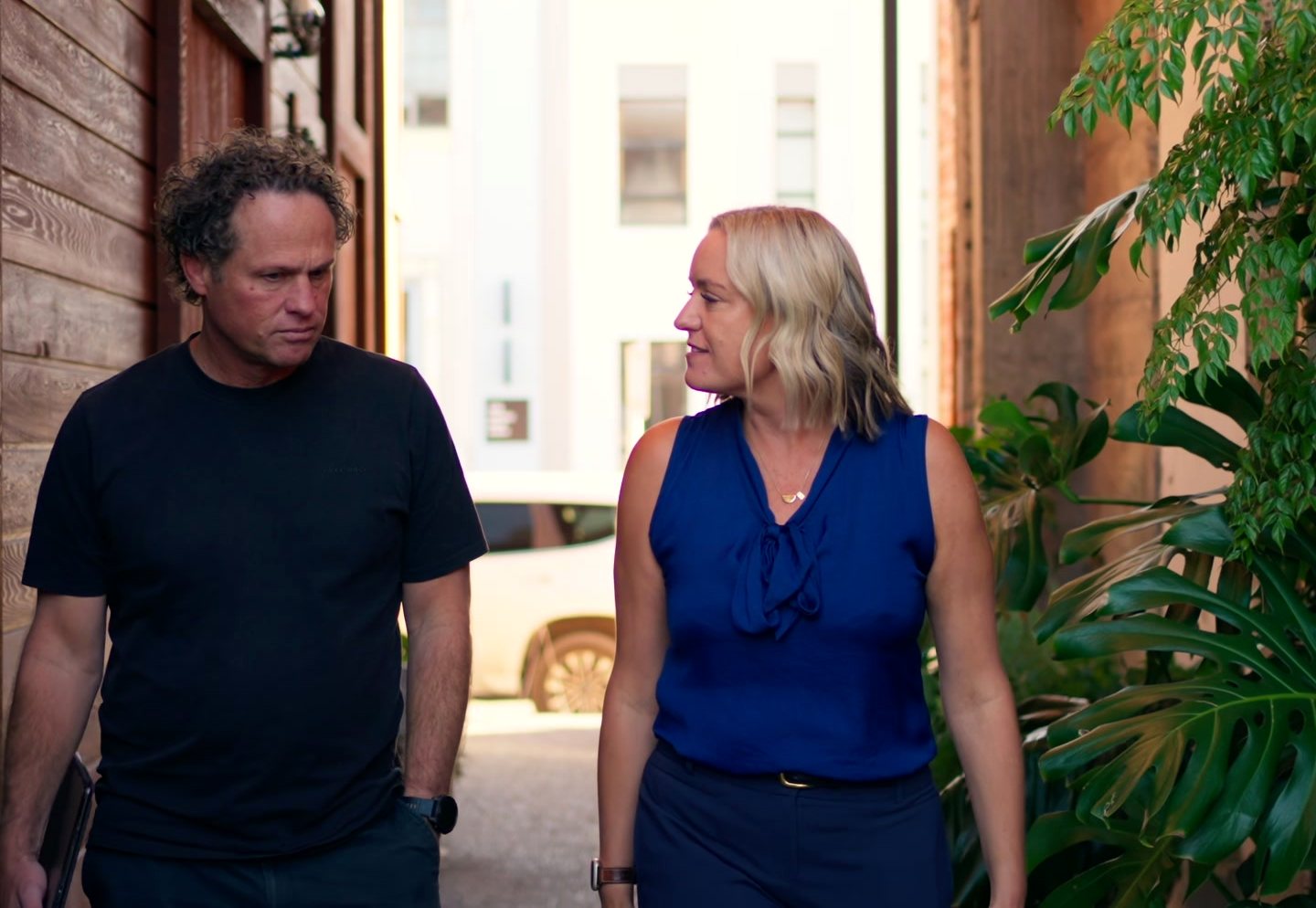 Matt and Mell walking out through a doorway lined with plants